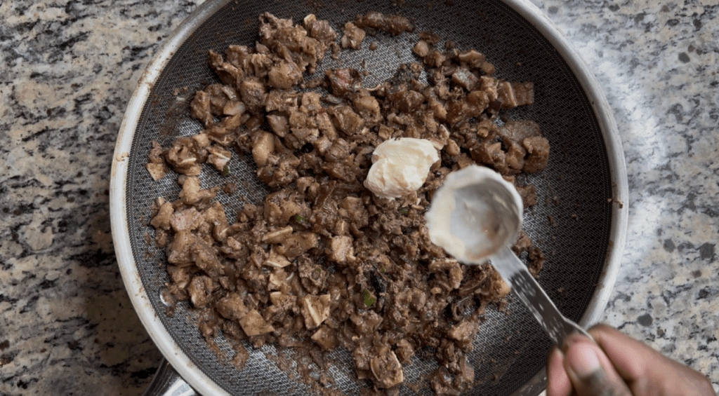 A close-up view of a frying pan with cooked, minced meat and a dollop of butter on top, set on a granite countertop.