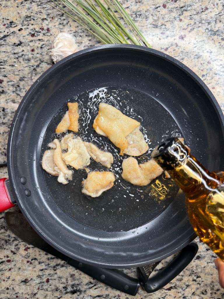 Frying pieces of food in a round frying pan on a granite countertop with a bottle being poured in.