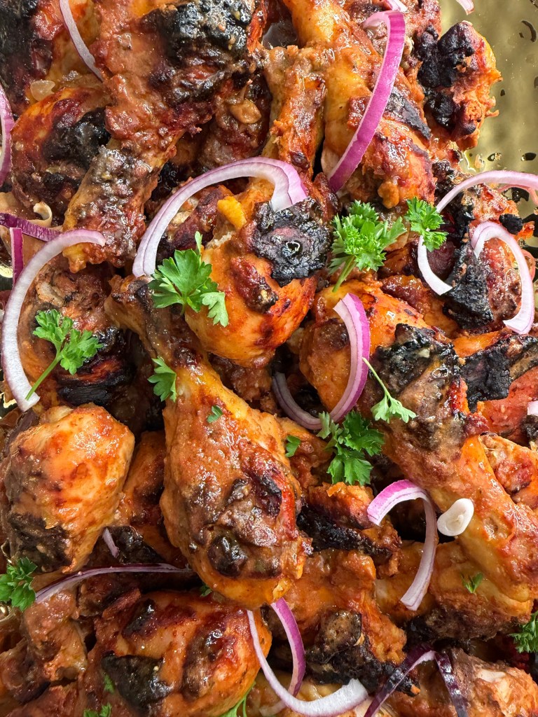 A close-up view of grilled chicken drumsticks garnished with slices of red onion and fresh parsley.