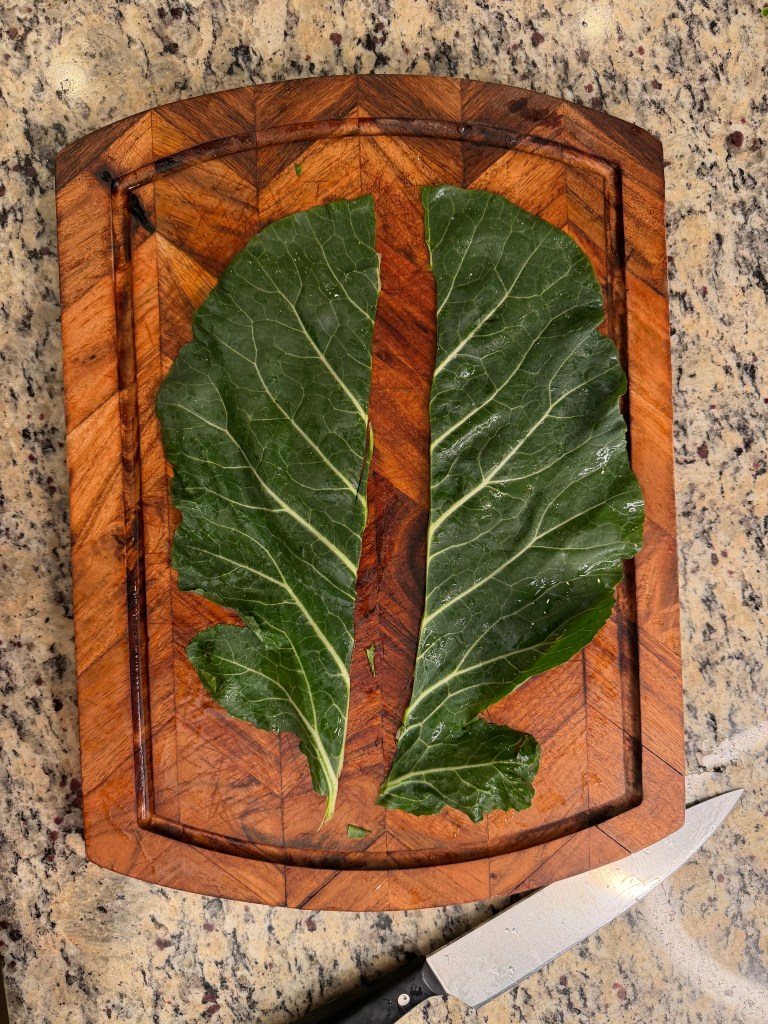 Two large collard green leaves placed on a wooden cutting board with a knife visible alongside.