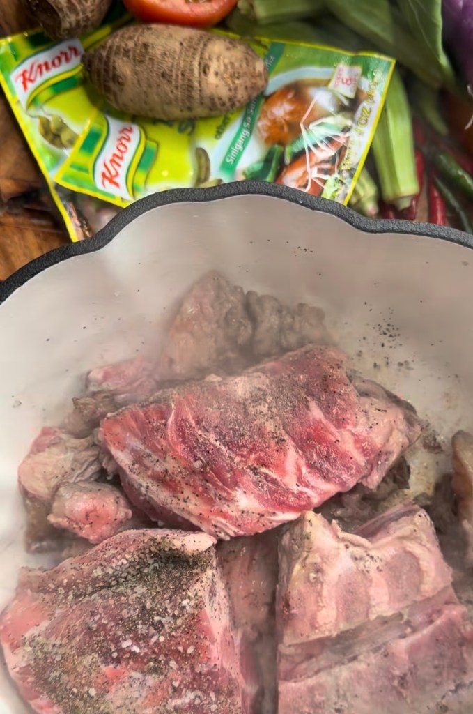 Close-up view of seasoned meat chunks in a pot, with background ingredients including vegetables and seasoning packets.