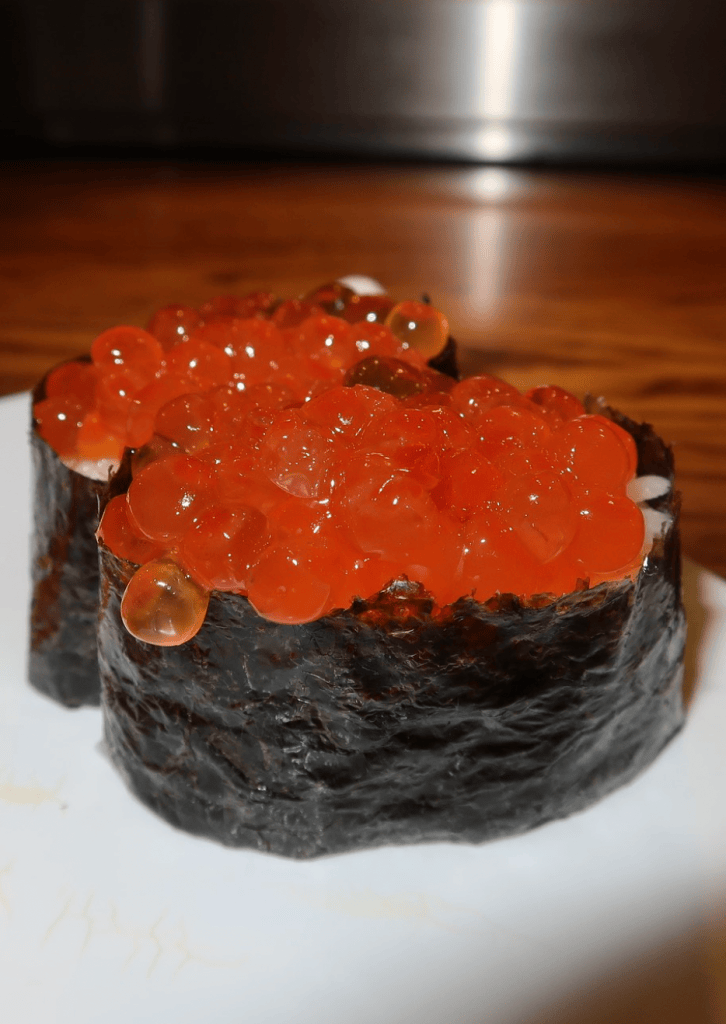 A close-up of sushi topped with bright orange fish roe, served on a white plate.