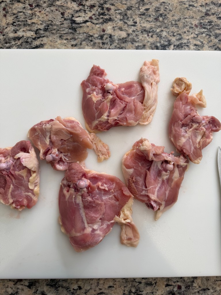 Raw chicken thighs arranged on a white cutting board, with a knife nearby.