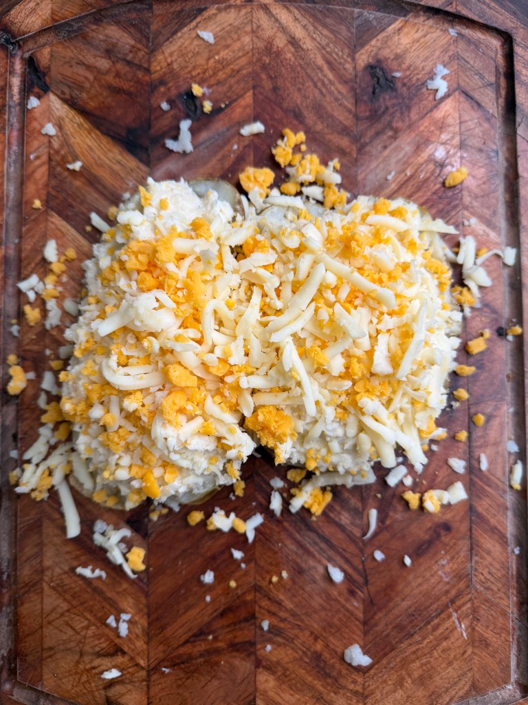 Shredded cheese on top of a creamy dish, served on a wooden cutting board.