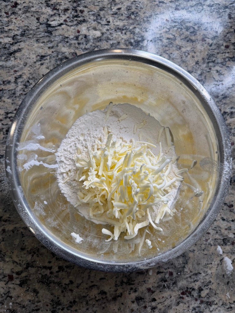 A mixing bowl containing flour and shredded cheese on a granite countertop.