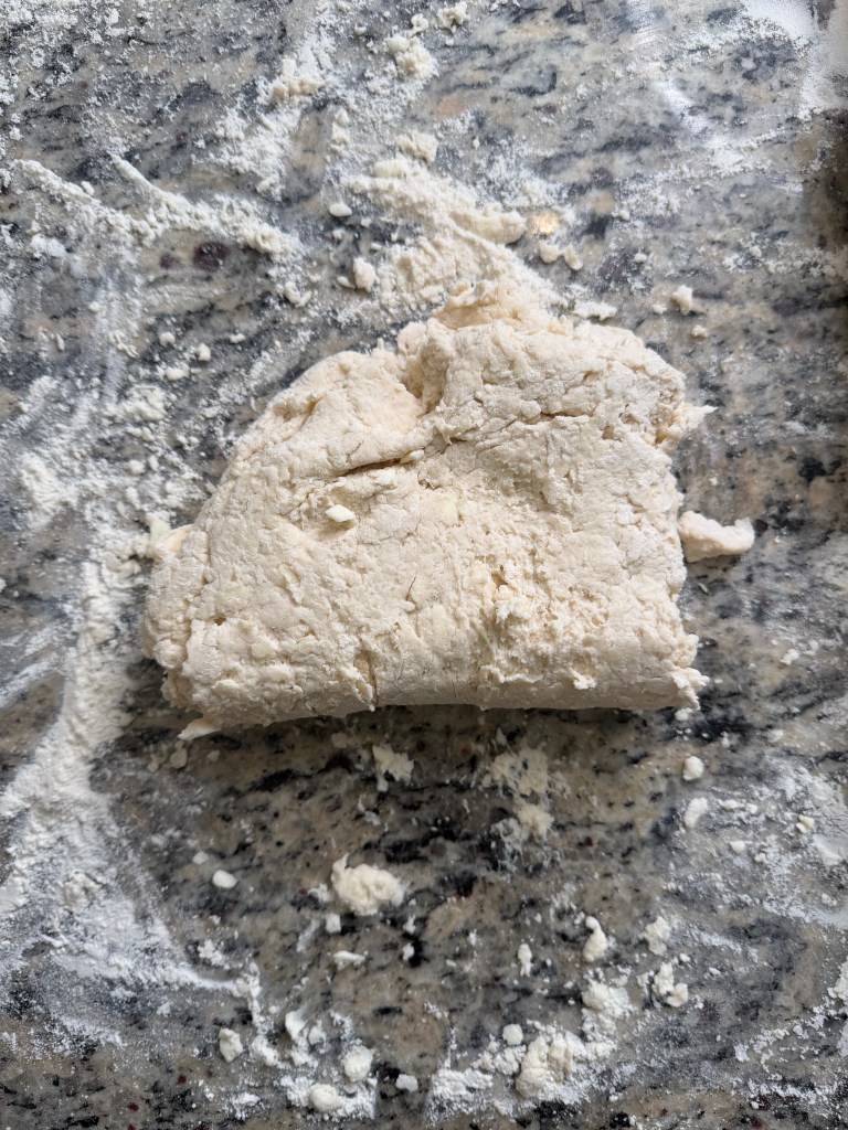 A piece of dough resting on a speckled granite countertop, surrounded by scattered flour.