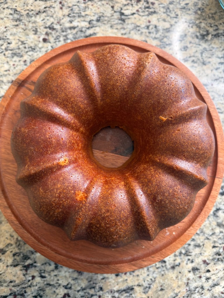 A freshly baked bundt cake resting on a wooden platter against a granite background.