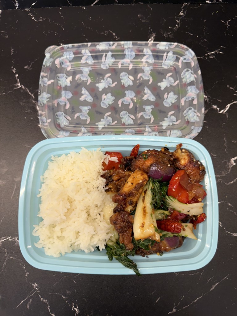 A portion of rice served with a stir-fried chicken and vegetable dish in a blue takeout container, topped with a patterned lid.
