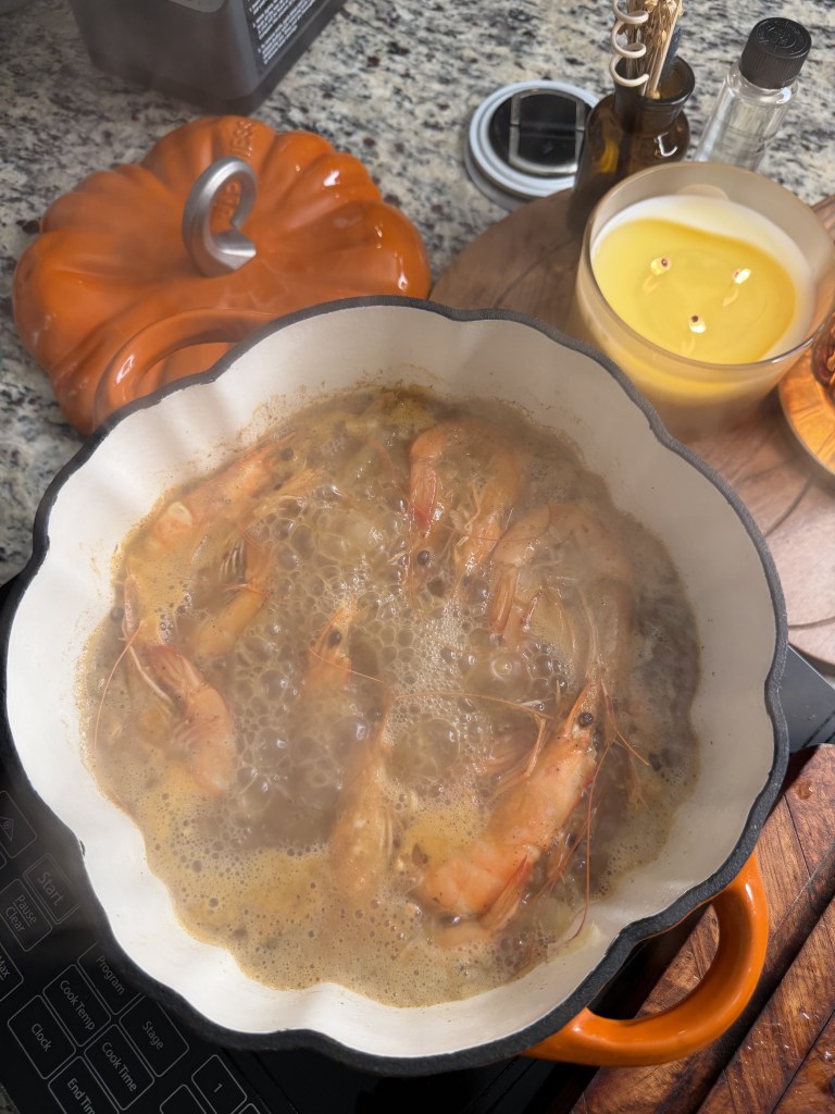 A pot of boiling shrimp in a creamy broth, surrounded by a pumpkin-shaped lid, a candle, and various kitchen items.