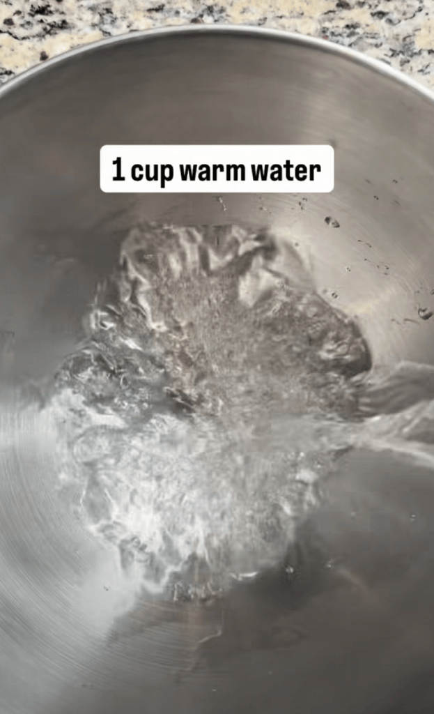A close-up view of one cup of warm water being poured into a stainless steel bowl.