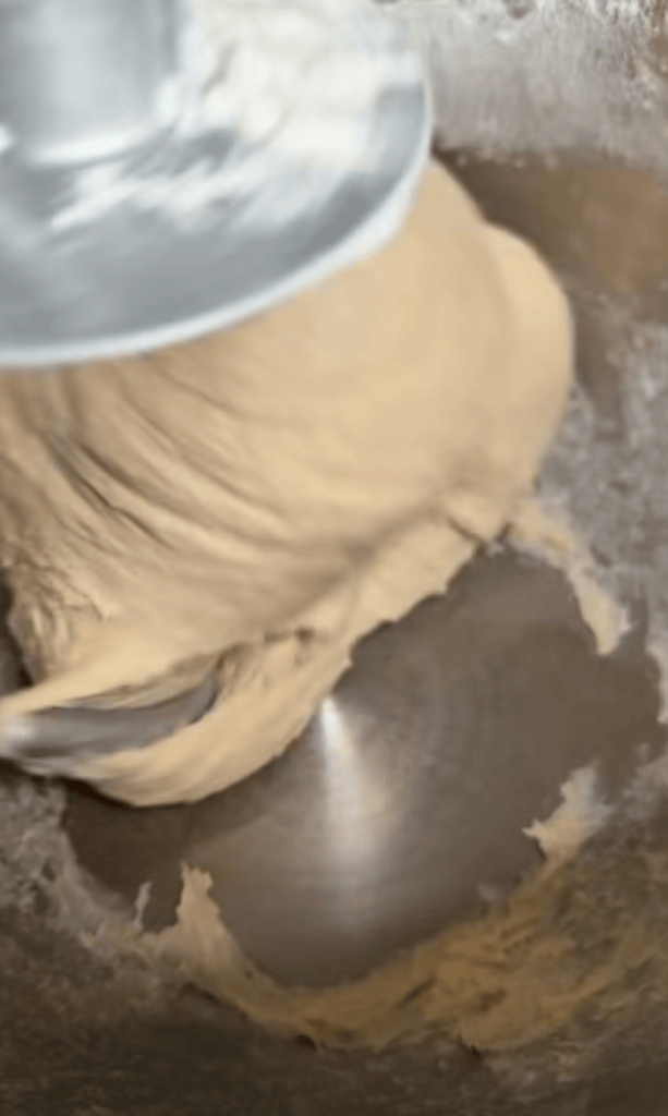 Close-up of dough being mixed in a metal bowl with a mixer attachment.