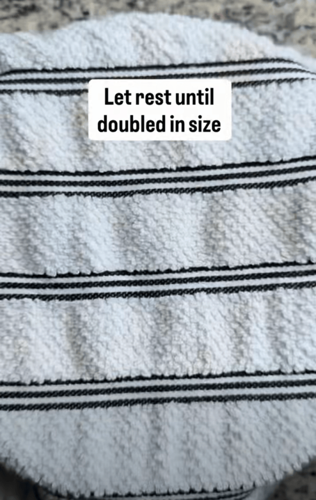 A kitchen countertop with a white towel featuring black stripes, topped with a caption that reads 'Let rest until doubled in size'.