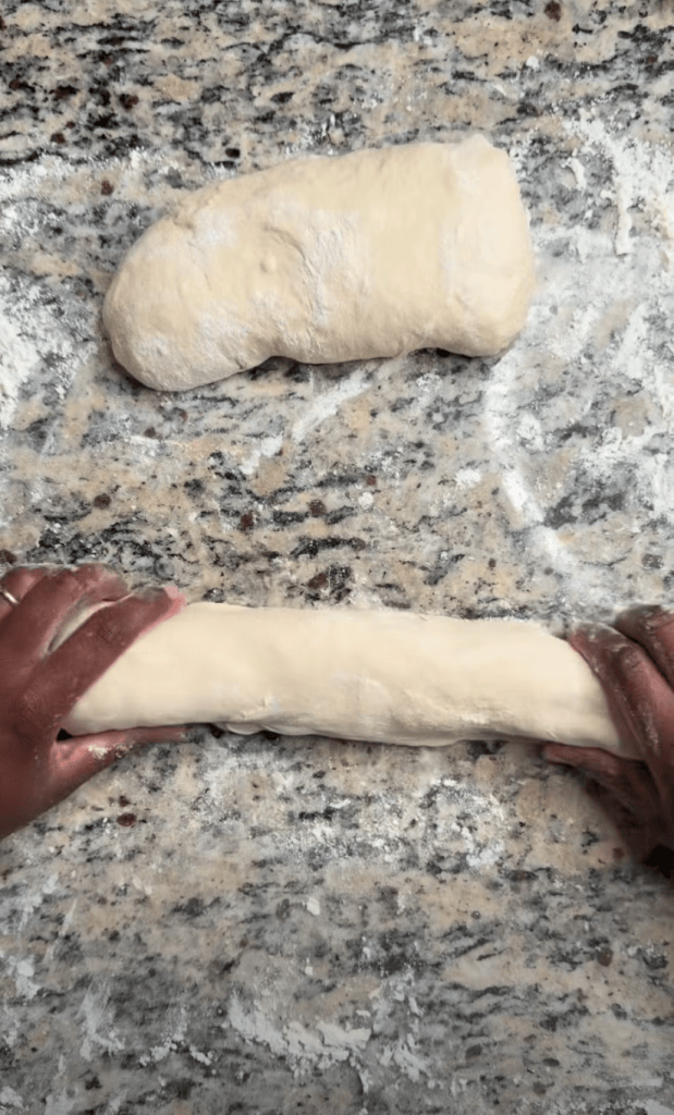 Hands rolling dough on a floured countertop with a second piece of dough in the background.