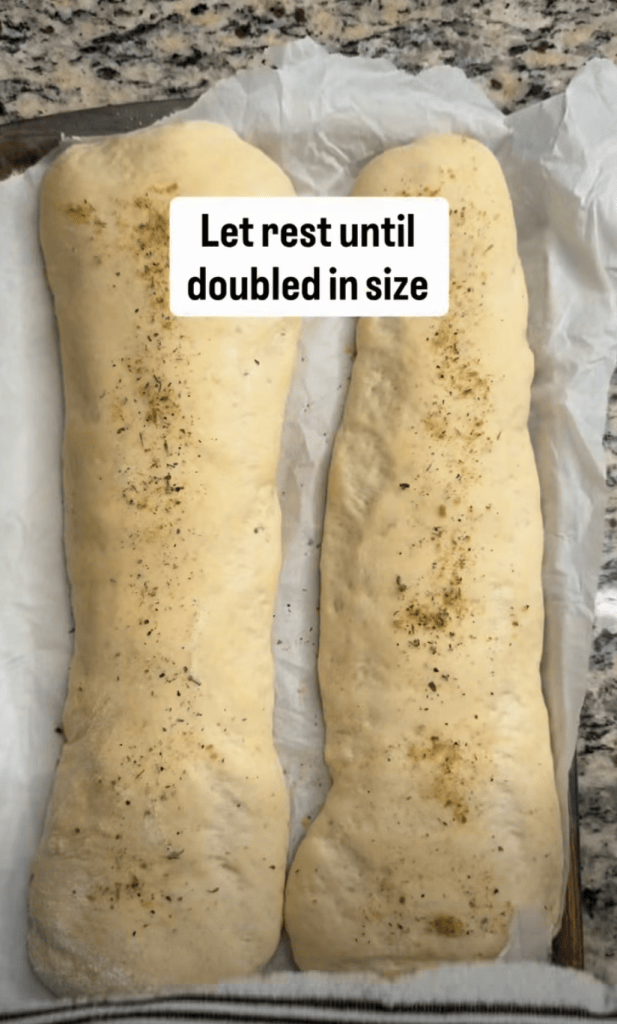 Two pieces of dough resting on parchment paper, sprinkled with herbs, with a note indicating to let them rest until doubled in size.