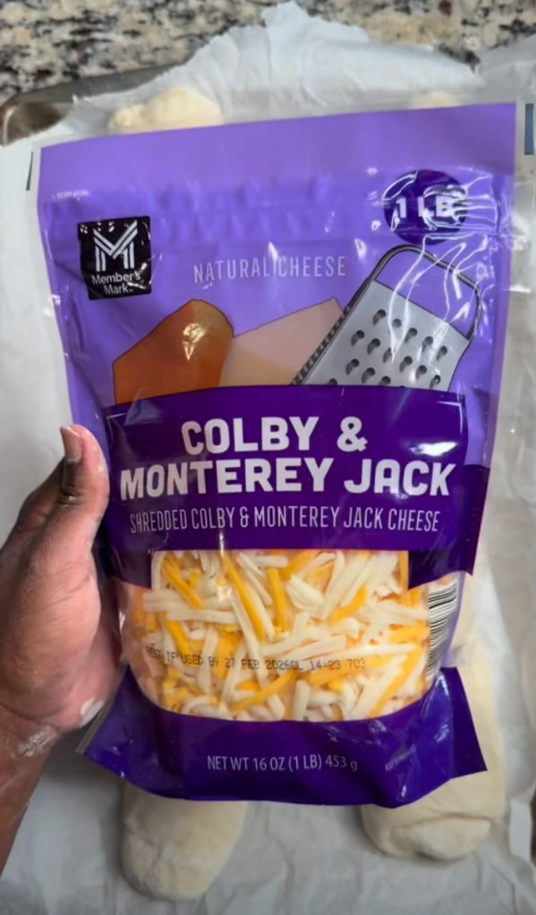A person holding a bag of shredded Colby and Monterey Jack cheese, featuring purple packaging with the brand name 'Member's Mark'.