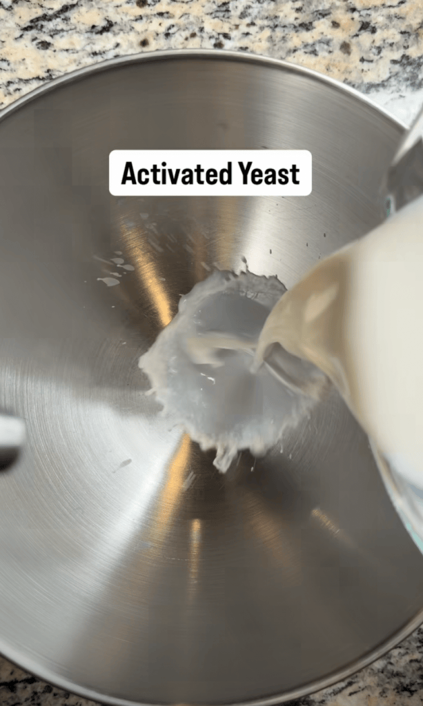 Pouring activated yeast into a mixing bowl on a granite countertop.