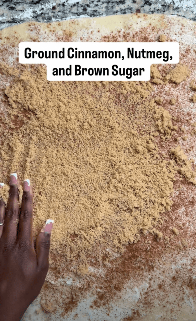 A hand resting on a surface covered with ground cinnamon, nutmeg, and brown sugar.