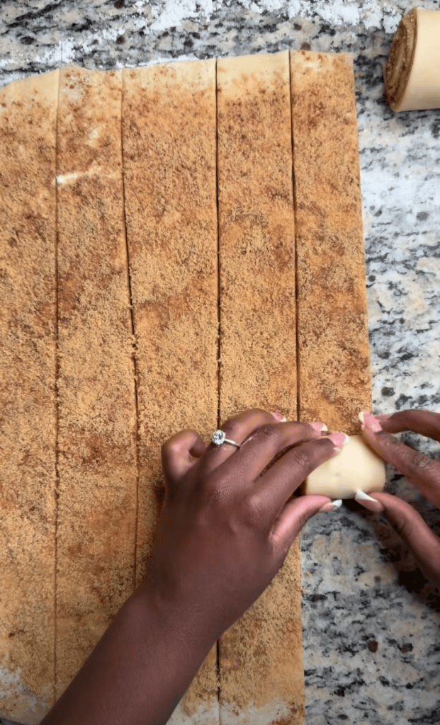 A person rolling a dough filled with cinnamon and sugar on a granite countertop.