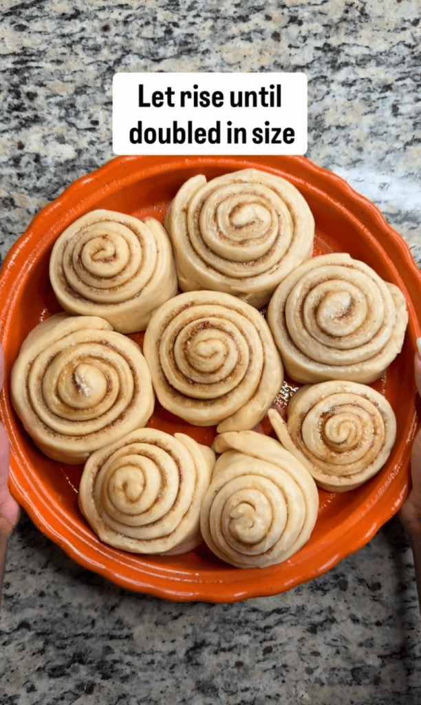 A plate of unbaked cinnamon rolls arranged in a circular pattern, with a text overlay instructing to let them rise until doubled in size.
