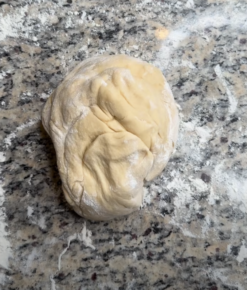 A ball of dough resting on a granite countertop, sprinkled with flour.