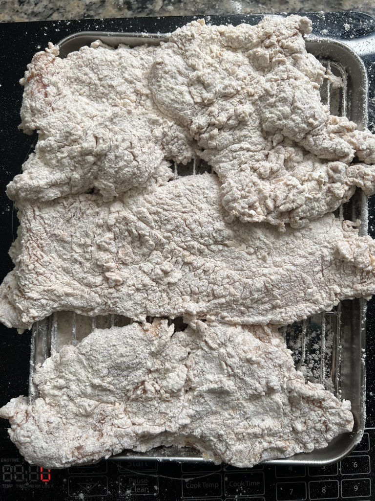 Raw meat coated in flour on a cooling rack, prepared for frying.