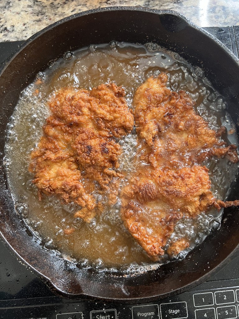 Frying chicken in a cast iron skillet with bubbling oil.
