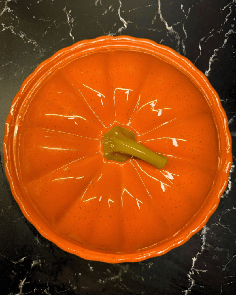 An orange pumpkin-shaped bowl with a green stem, placed on a black marble surface.